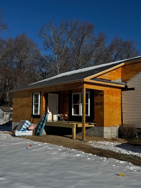 House under construction with exposed wood siding and porch, set in a snowy yard.