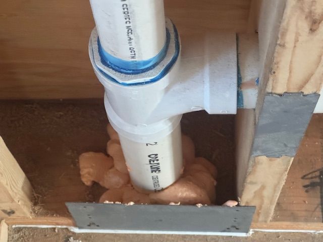 PVC plumbing pipes joined with a T-fitting, sealed with expanding foam, and set in a wooden frame.