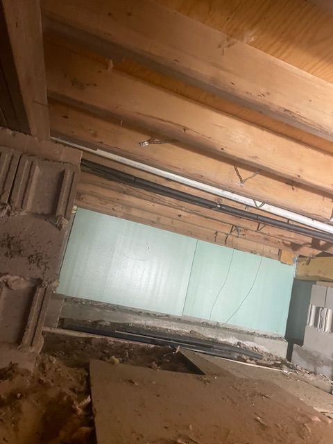 Interior shot of an unfinished space showing wooden beams, insulation, and exposed building materials.