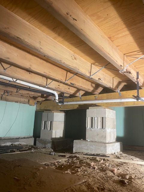 View of a crawl space with concrete support pillars and wooden beams holding up a house.