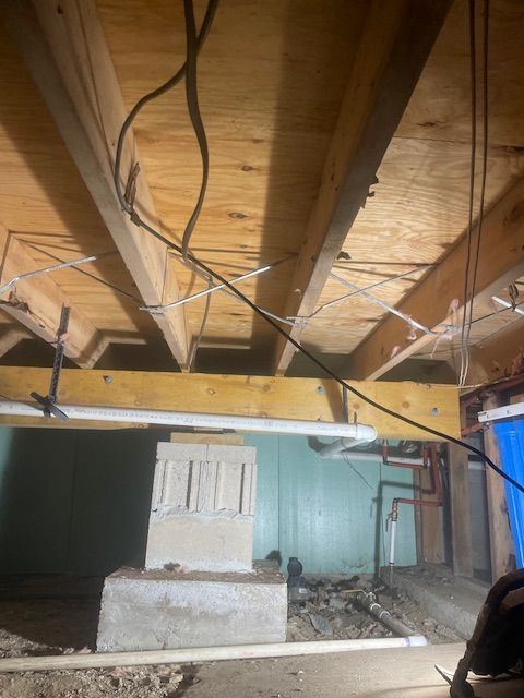 View from below of exposed beams, pipes, and wiring in a crawl space.