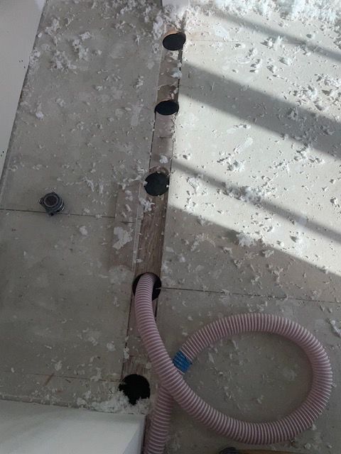 Construction site with a concrete floor. A line of circular holes and a pink corrugated tube are visible.