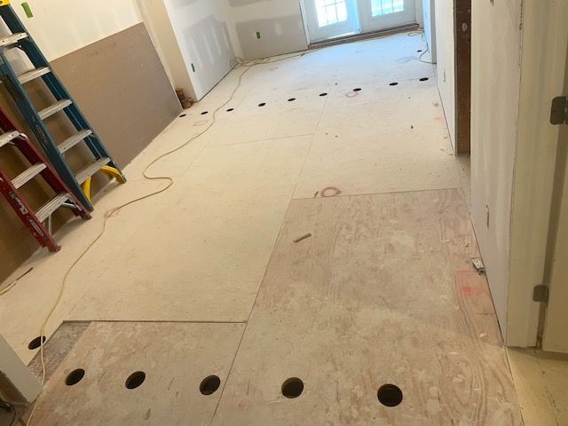 Interior view of a room under construction with plywood flooring, drilled holes, ladders, and drywall.