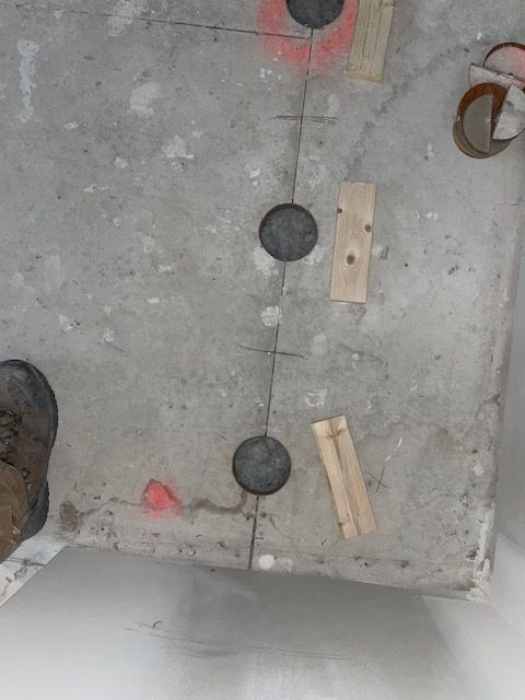 Concrete surface with three dark holes and wood pieces; a foot visible.