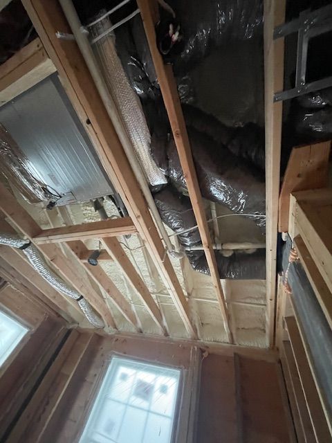 View of a ceiling with wooden beams, insulation, and ductwork, inside a house under construction.