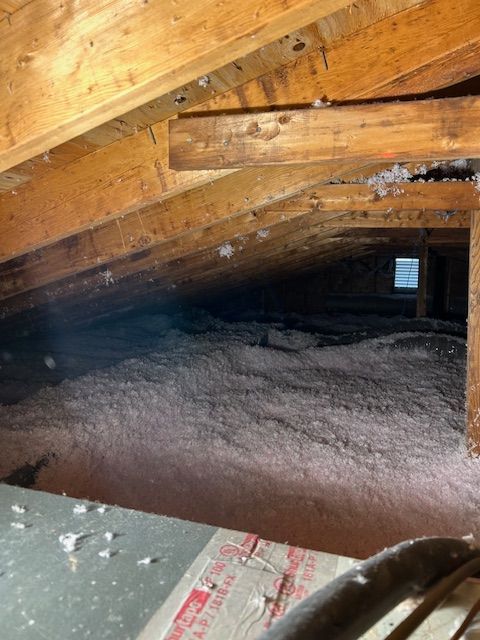 Attic space with pink insulation between wooden beams and rafters.
