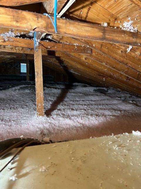 Attic space with pink insulation between wooden beams and rafters; blue pipe visible.
