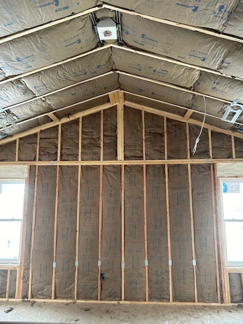 Interior view of a building under construction, featuring wooden framing, insulation, and windows.