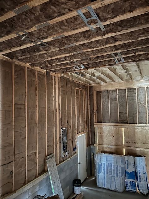 Interior view of a room under construction with exposed wooden framing, insulation, and stacks of insulation batts.