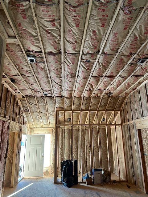Interior view of a building under construction, showing wooden framing, insulation, and door.