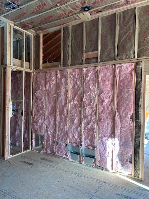 Interior wall under construction, framed with wood and insulated with pink fiberglass.