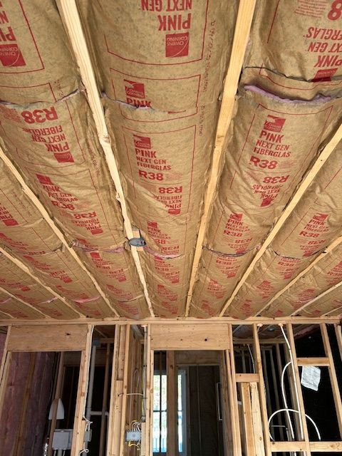 Interior view of a building under construction, showing ceiling insulation between wooden beams; R-38 pink insulation.