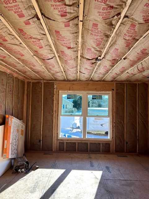Interior view of a room under construction with exposed wooden framing, insulation, and a window.