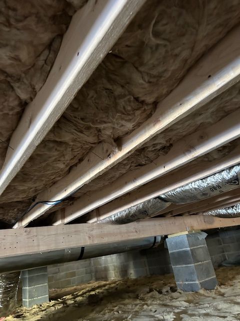 View from below of a crawl space with exposed beams, insulation, and cinder block supports.