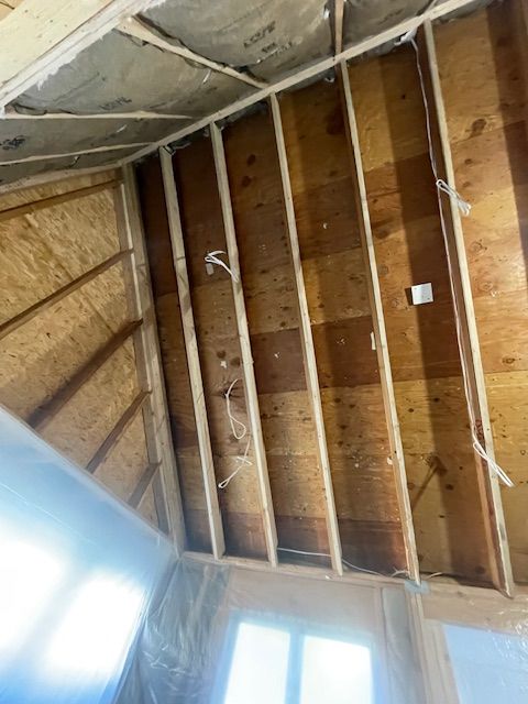 Partially stripped attic ceiling with exposed wooden rafters and insulation, viewed from below