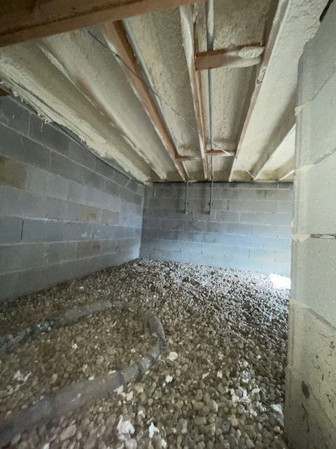 Unfinished crawl space with gravel floor, cinderblock walls, and exposed wooden ceiling joists.