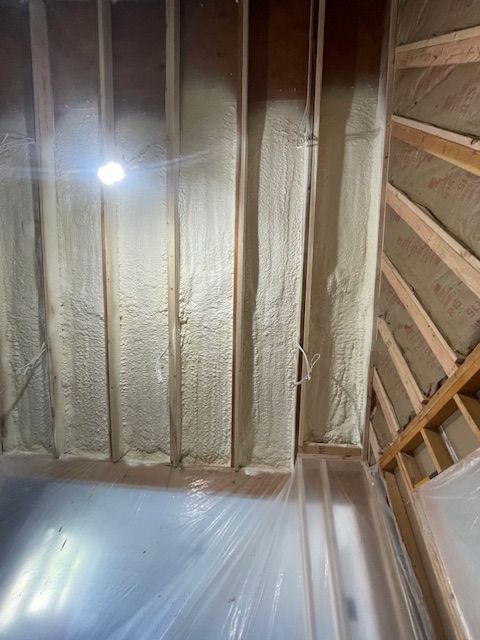 Insulated attic ceiling with exposed rafters, plastic sheeting, and a bright work light