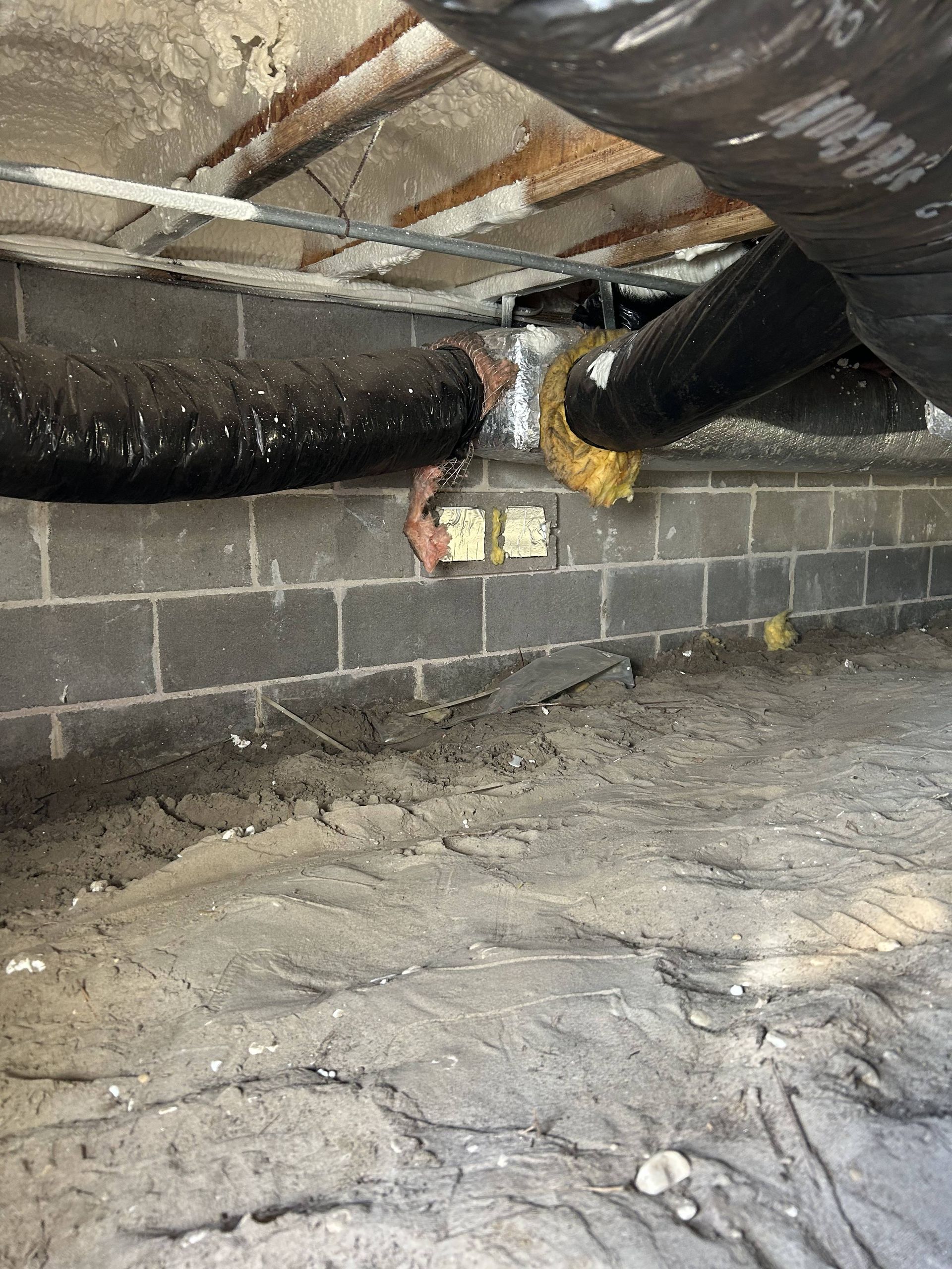 Basement crawlspace with exposed pipes, cinderblock wall, and an electrical box under a low ceiling
