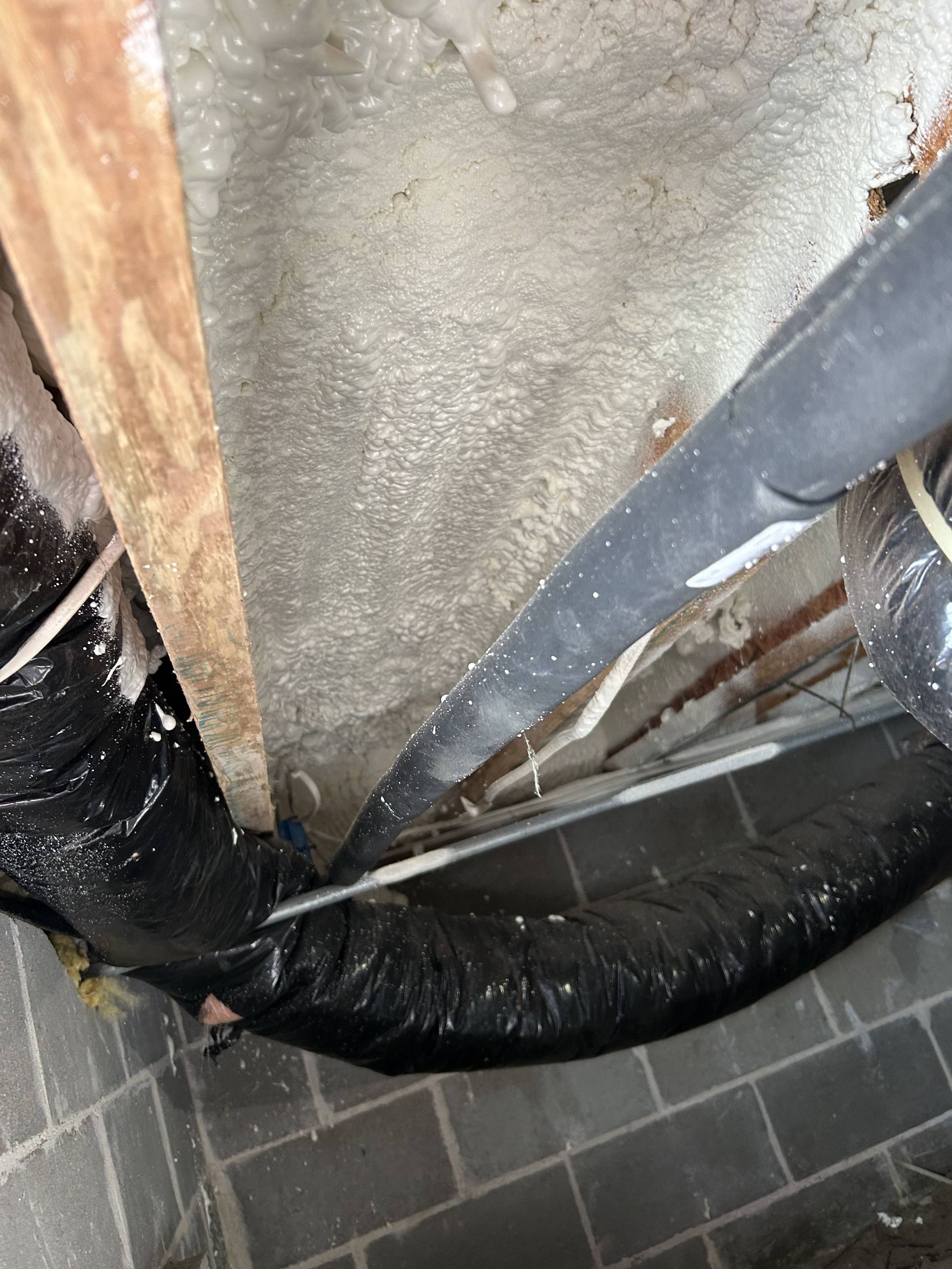 Damaged floor opening with exposed ductwork and insulation beside gray tile flooring