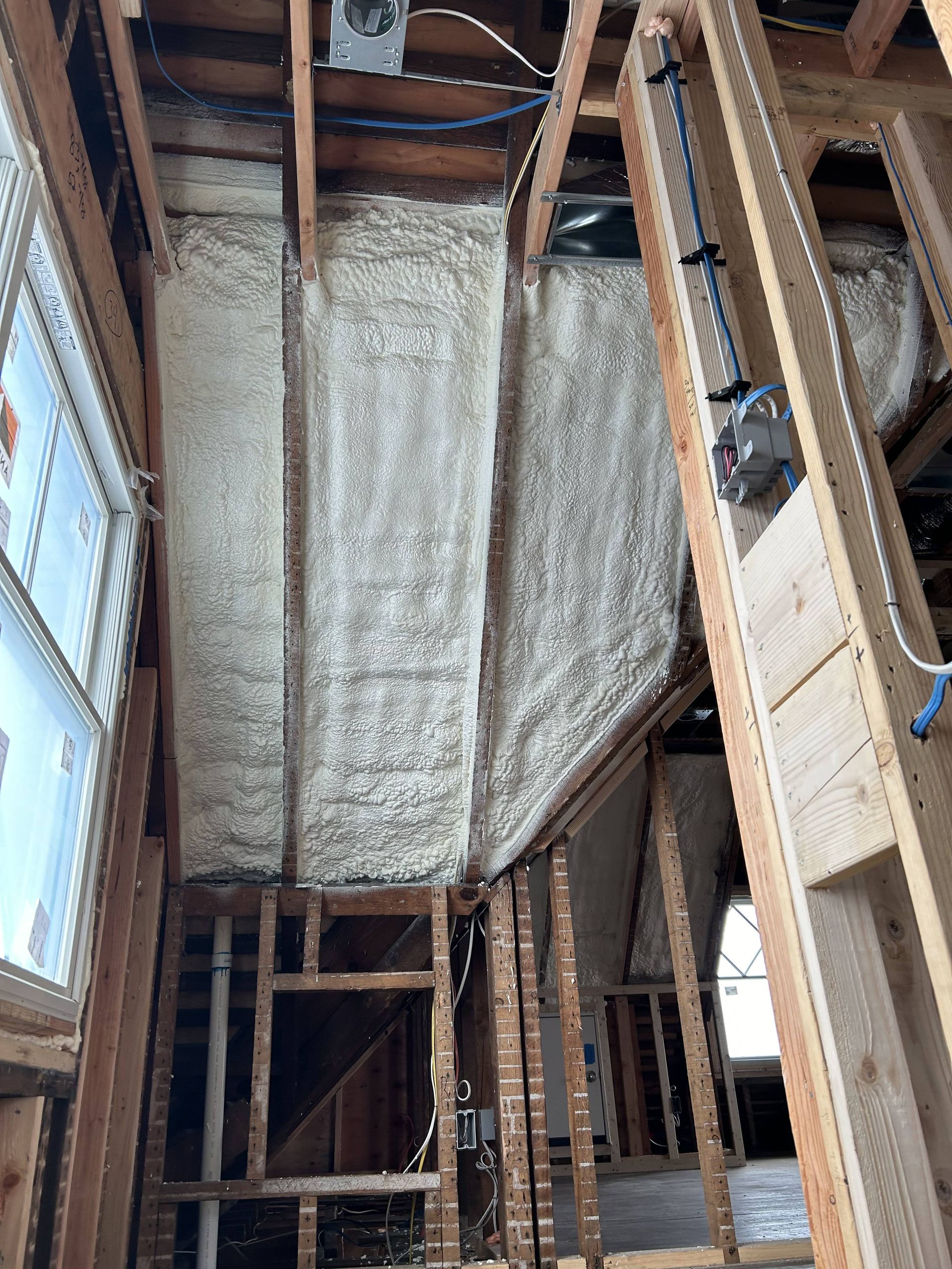 Interior of a house under construction with exposed framing and spray foam insulation on the ceiling and walls