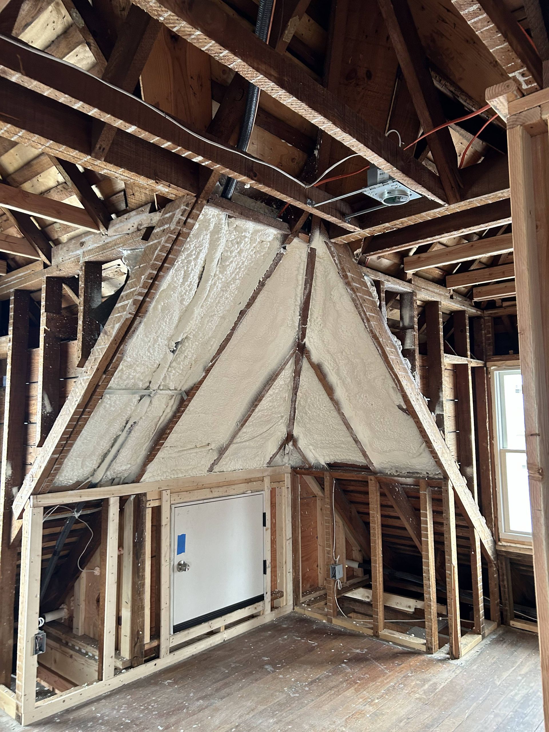 Destroyed interior with exposed roof beams, torn insulation, and a small framed alcove under construction or damage