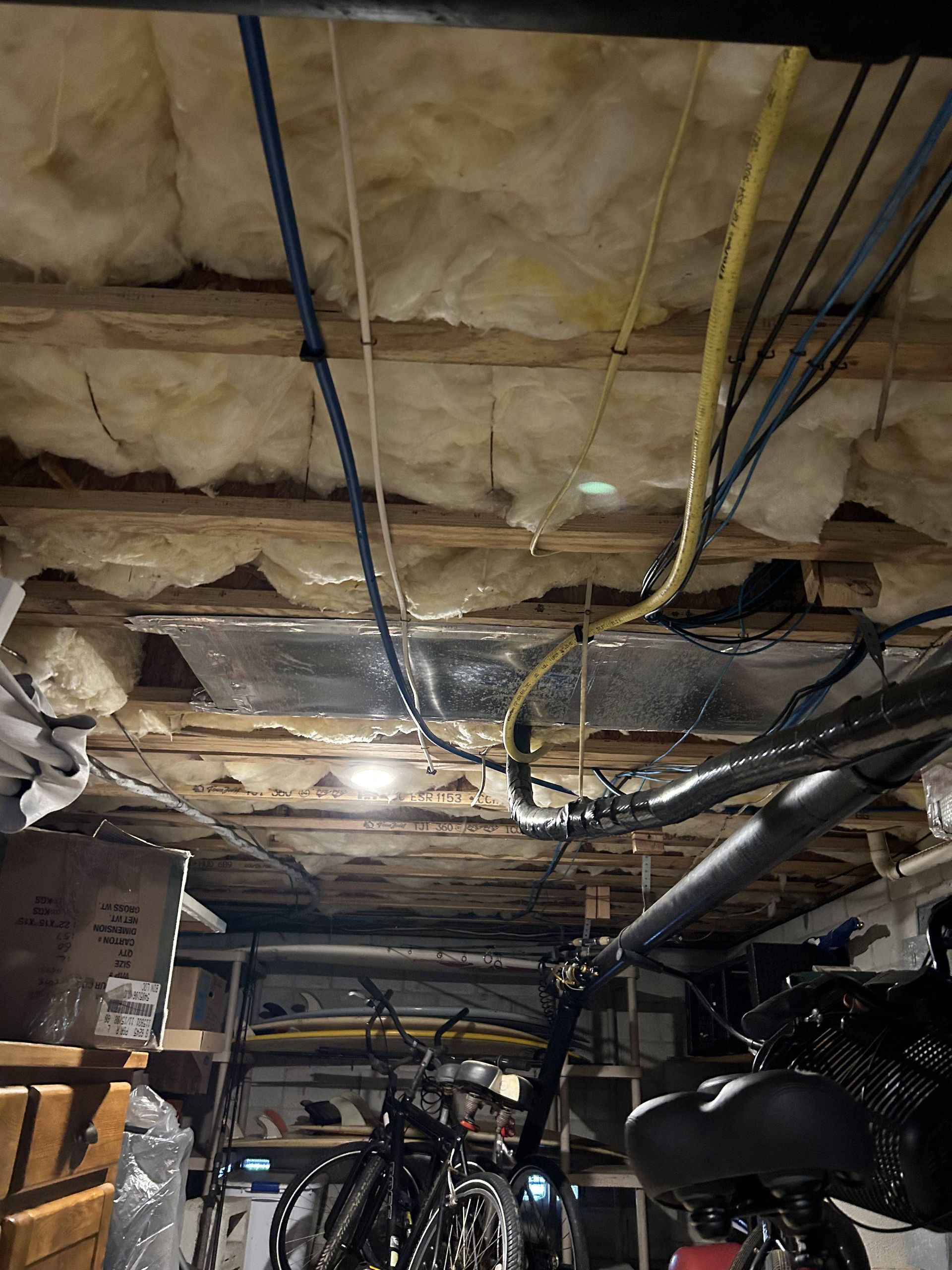 Partially insulated basement ceiling with exposed pipes, wires, and cluttered storage below