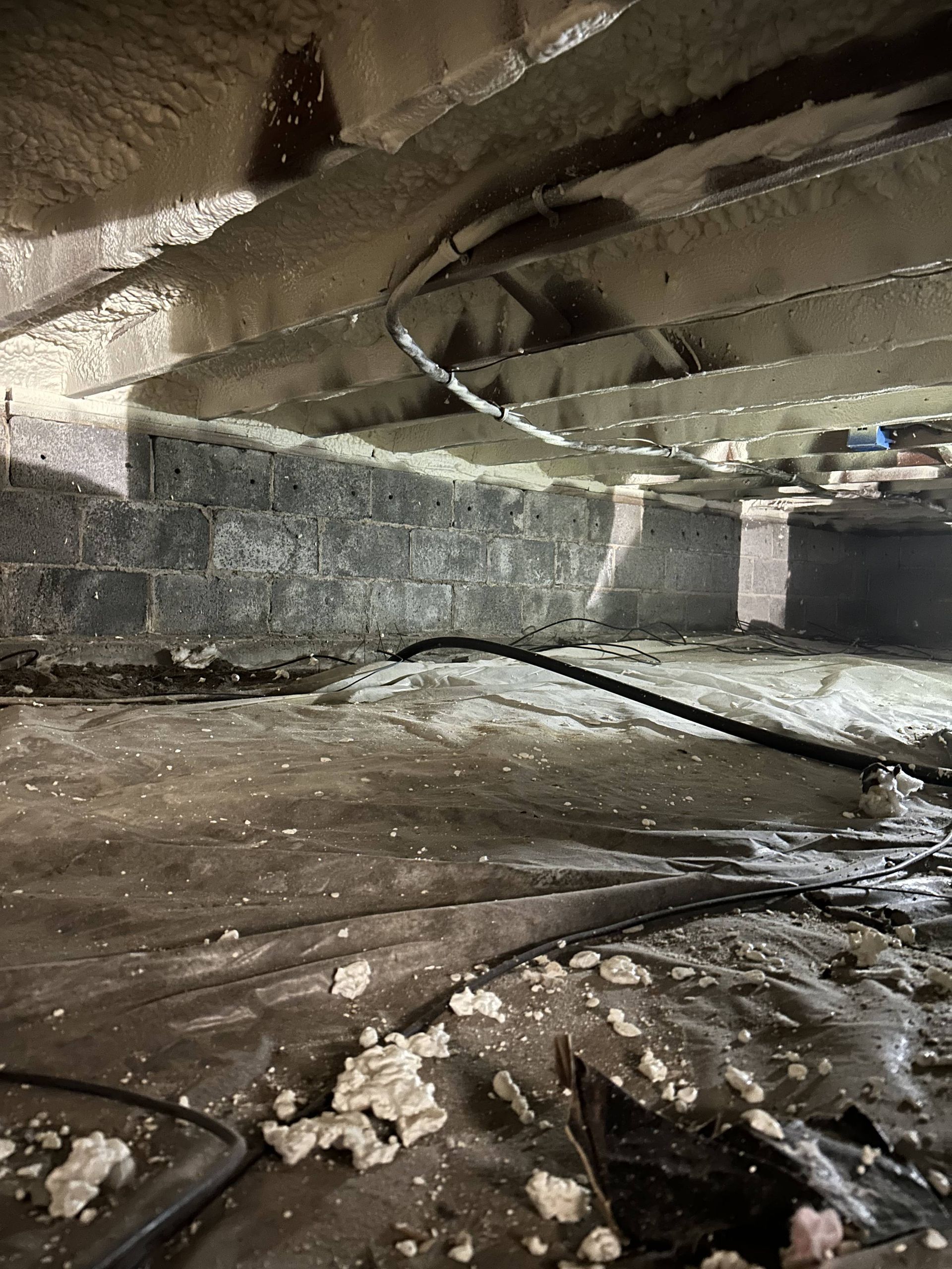 Flooded concrete basement with low ceiling, exposed beams, and debris on the wet floor