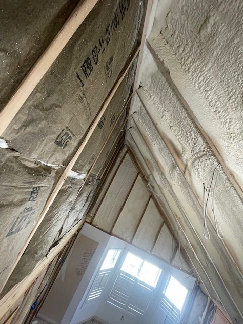 Attic interior with exposed insulation, roof beams, and a bright skylight at the far end