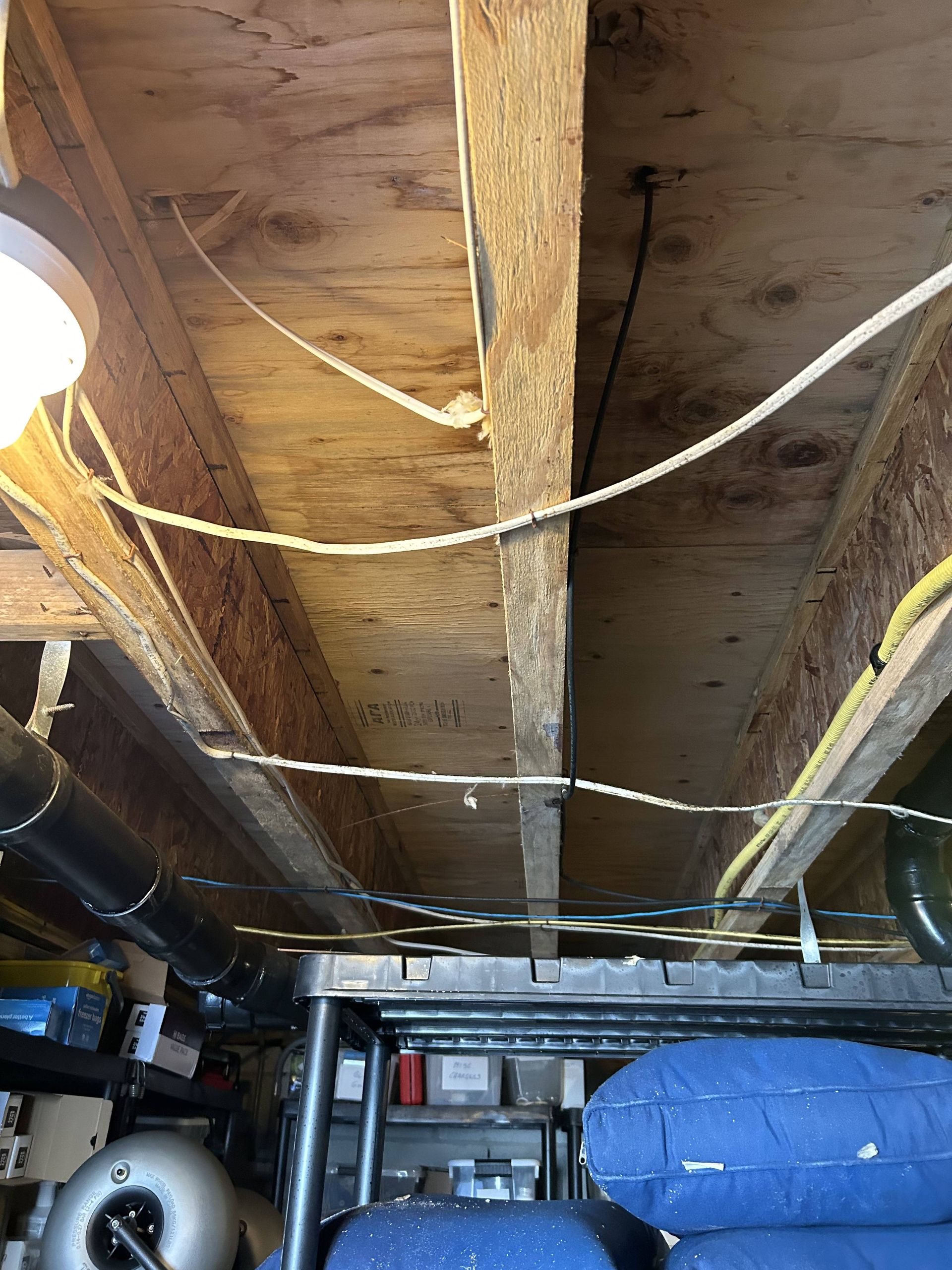 Basement ceiling with exposed wooden joists, hanging cables, and storage items below