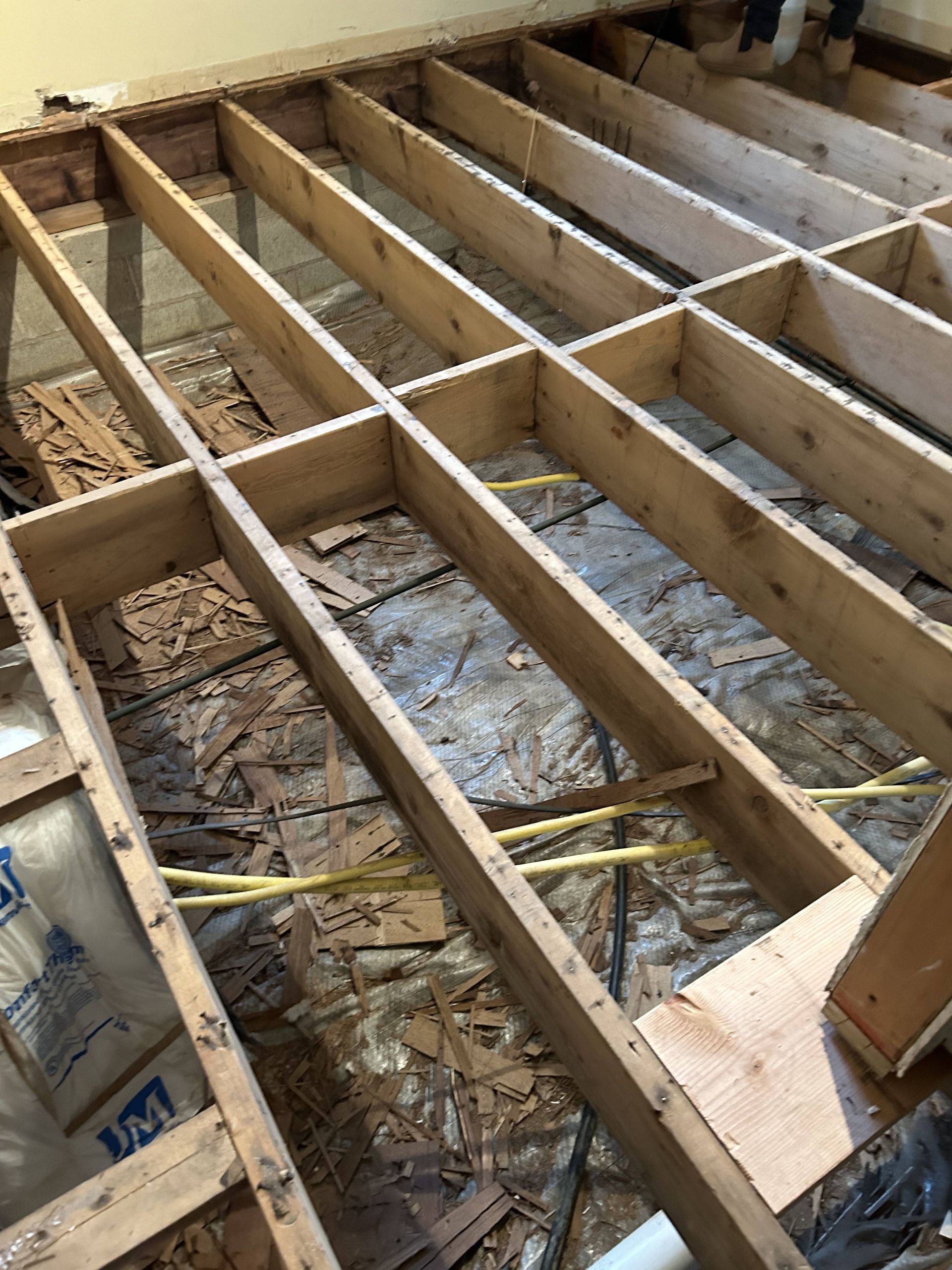 Exposed wooden floor joists and subfloor during home renovation, with insulation and wiring visible.