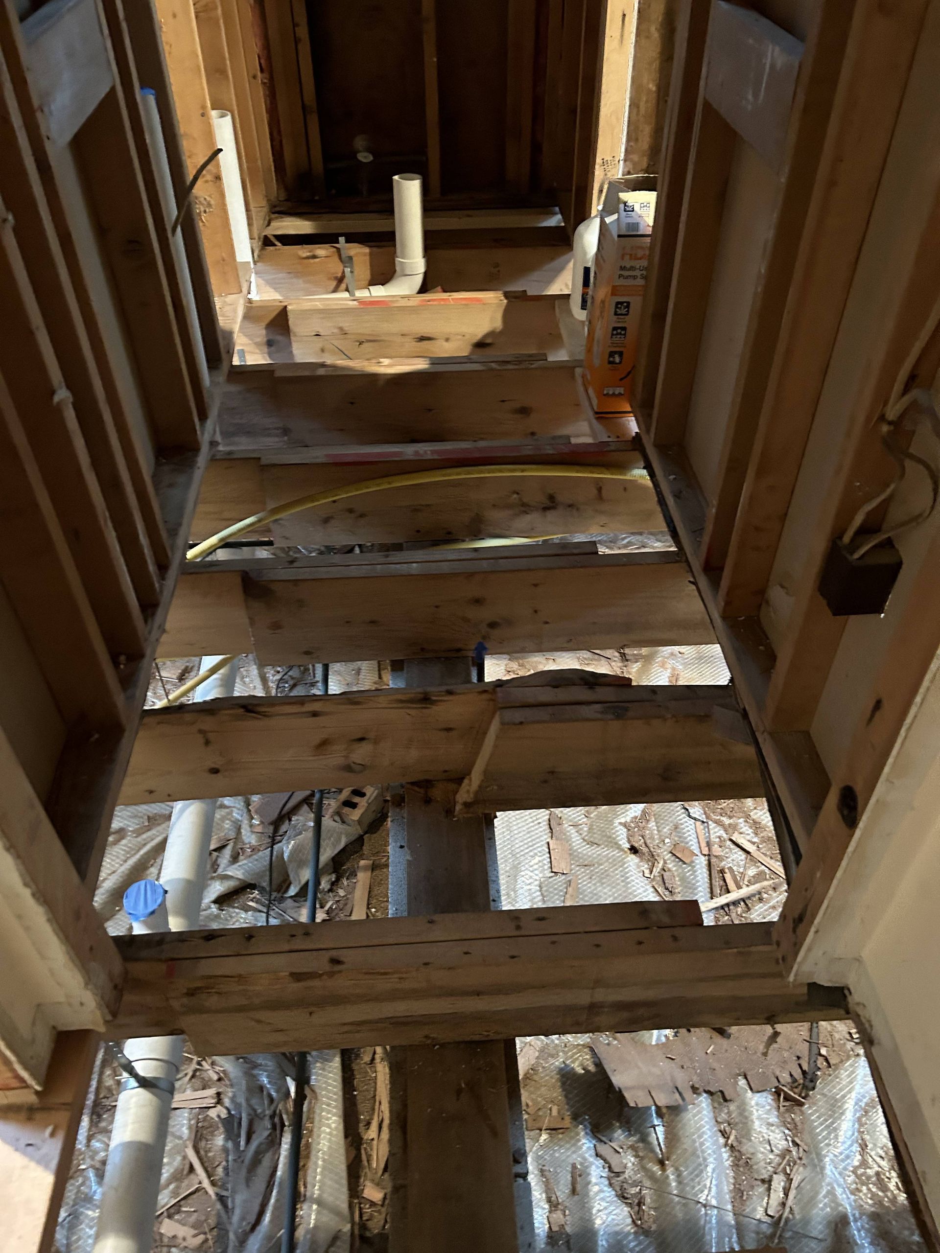 Exposed wooden framing and floor joists in an unfinished house interior, viewed upward through a narrow opening