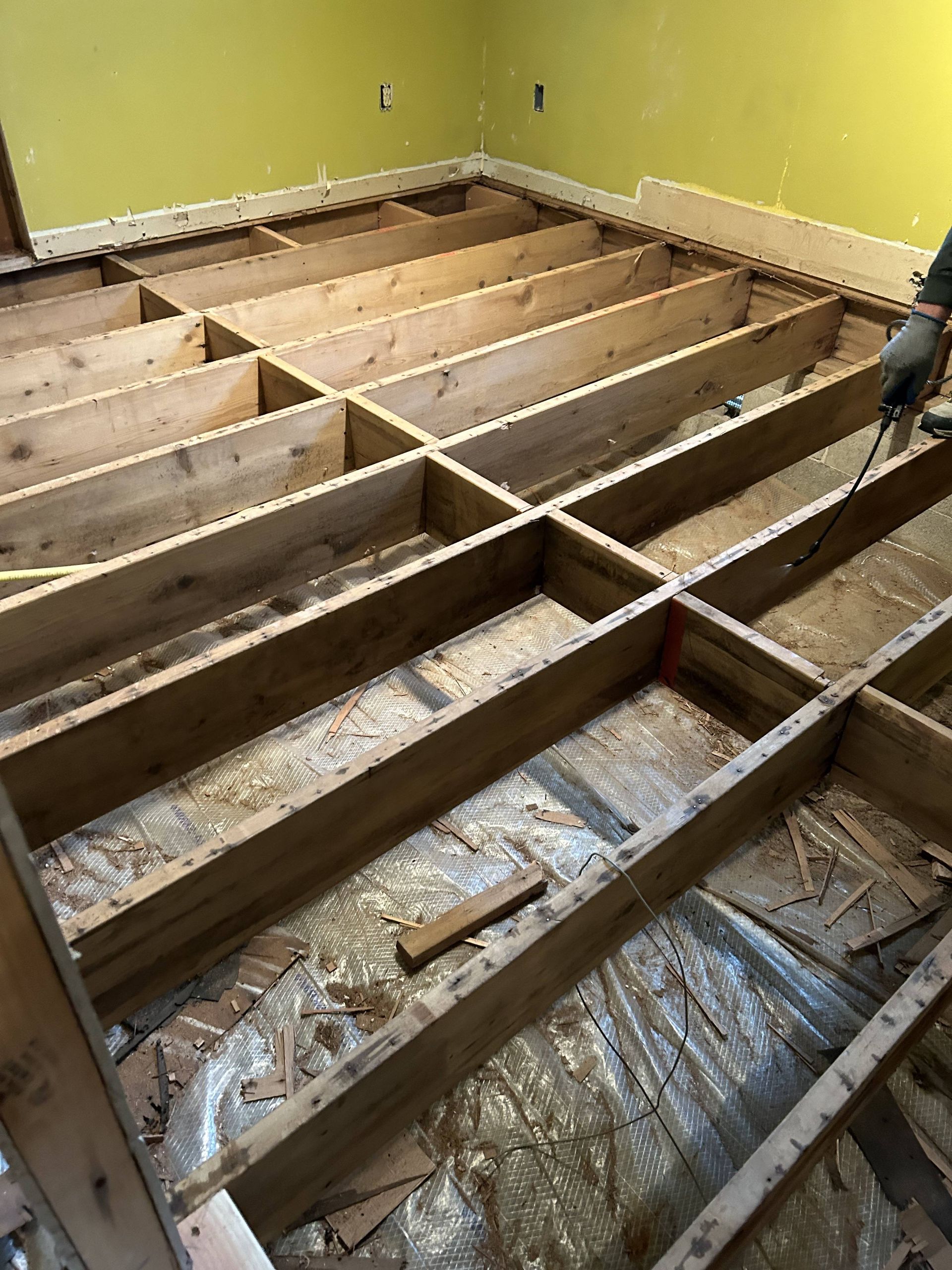 Exposed wooden floor joists in a room with yellow walls, under renovation