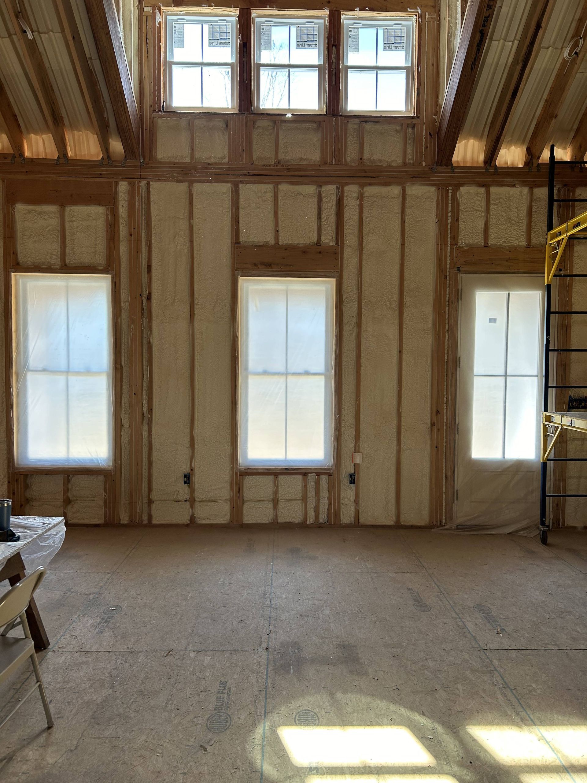 Empty unfinished room with exposed framing, tall windows, and sunlight on the floor
