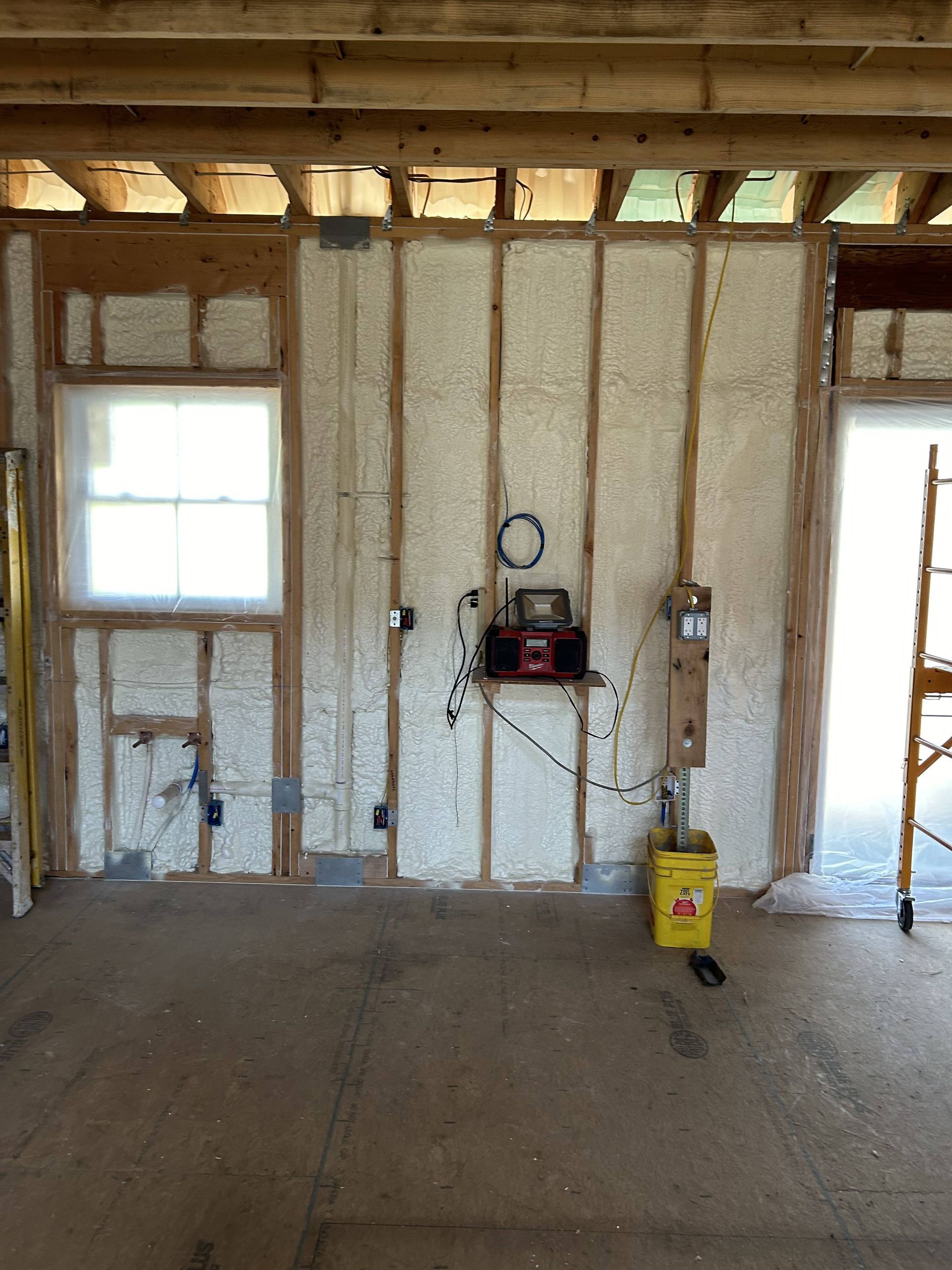 Unfinished room with exposed insulation, electrical wiring, a window, and tools on the floor.