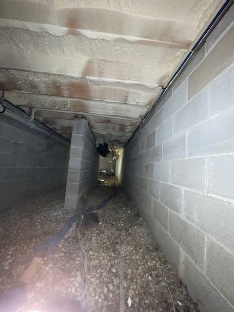 Narrow crawlspace with cinderblock walls, insulated ceiling, and gravel floor, lit from one end