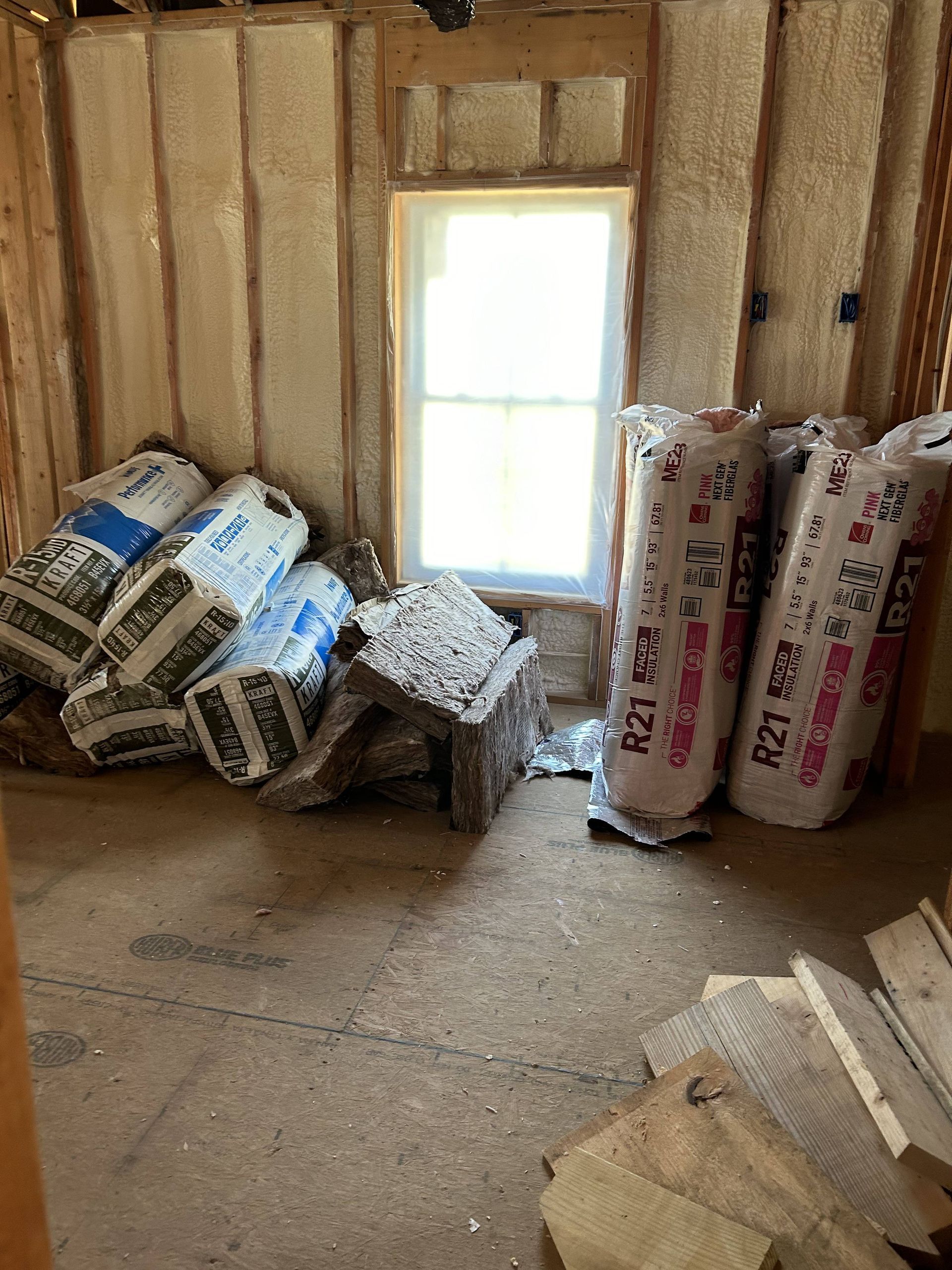 Insulated room with stacked rolls of flooring or insulation materials beside a window.