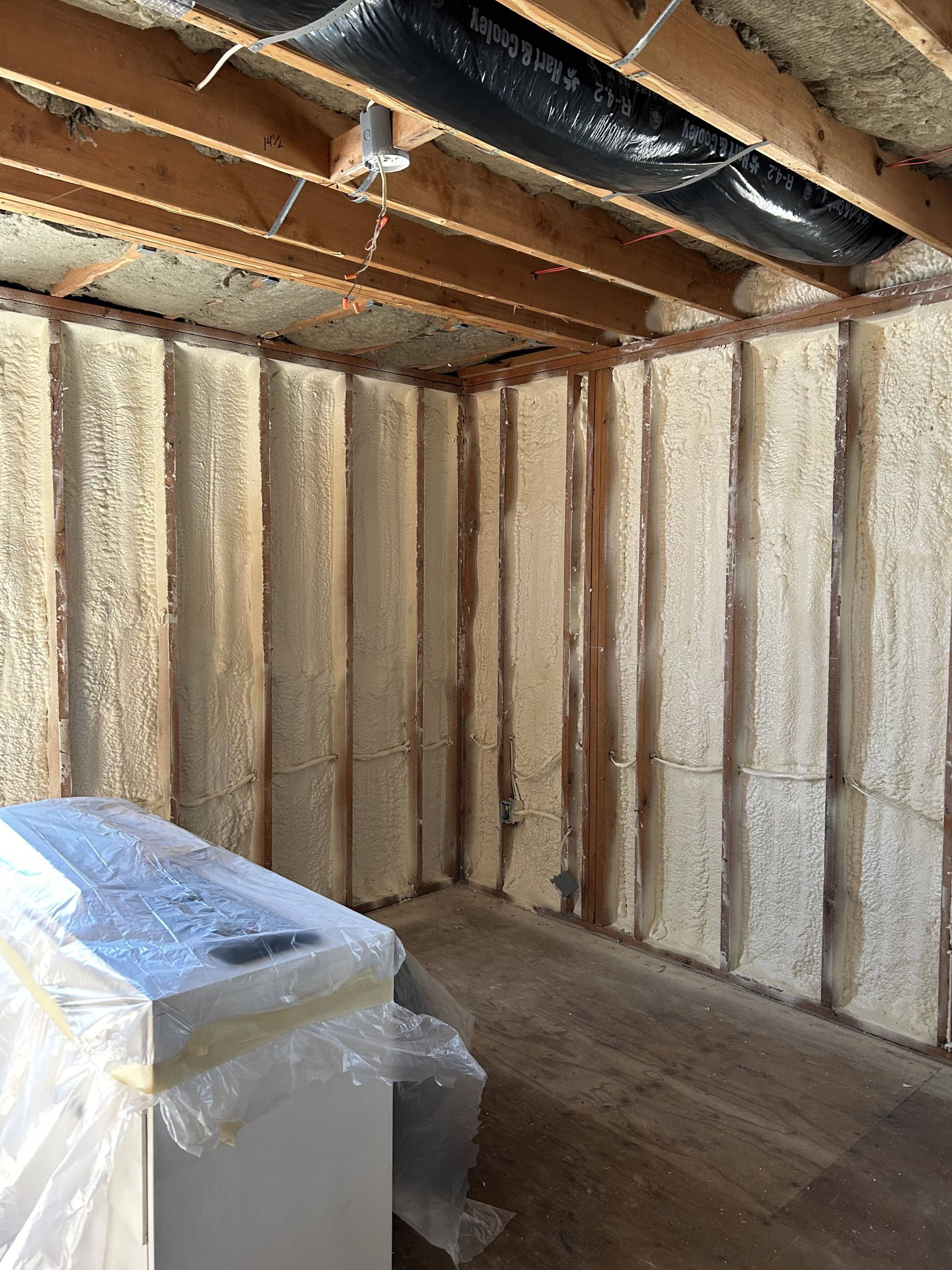 Unfinished basement wall with exposed insulation and a plastic-wrapped box on the floor.