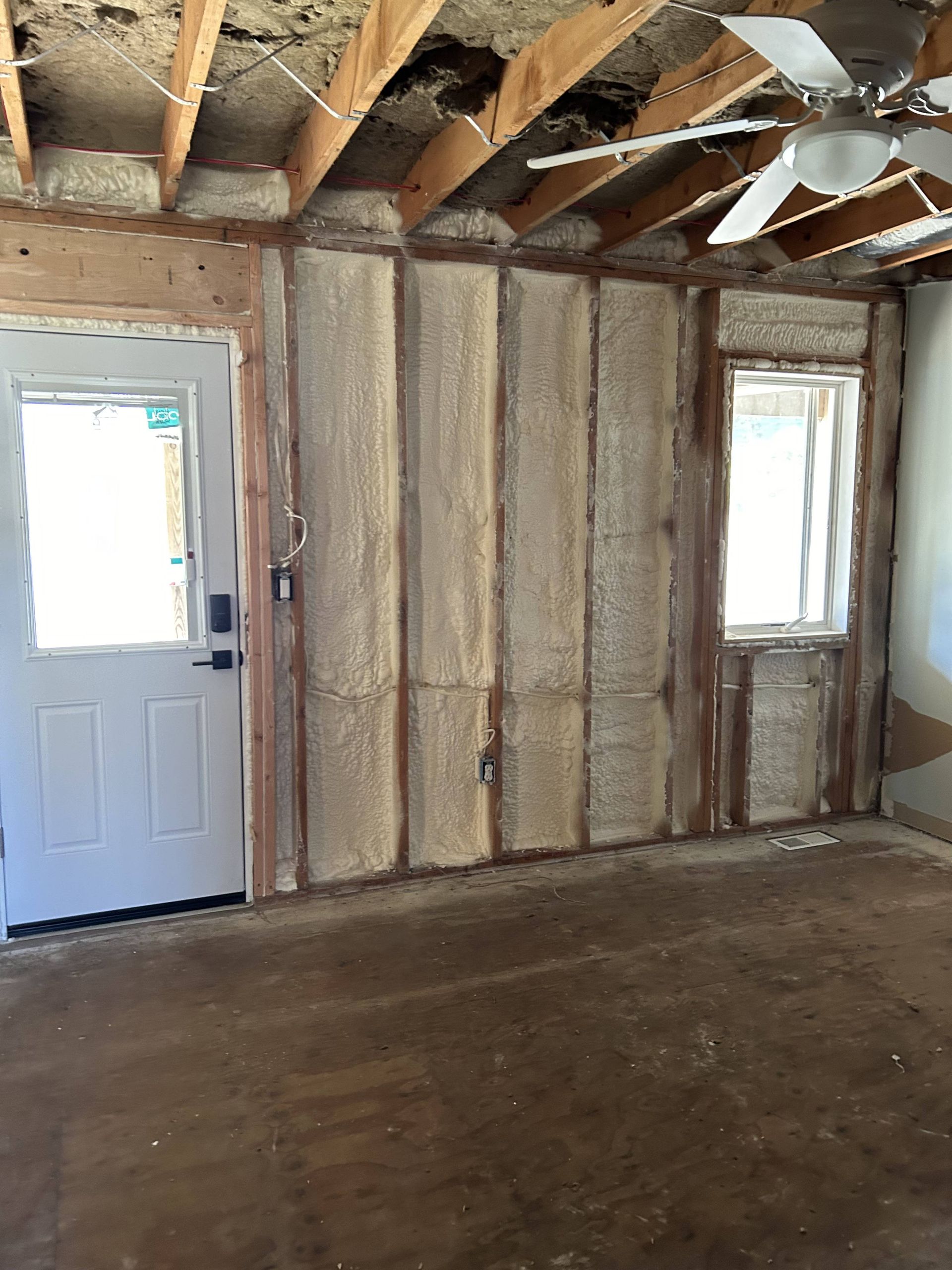Empty unfinished room with exposed wood framing, insulation, a white door, and a window.