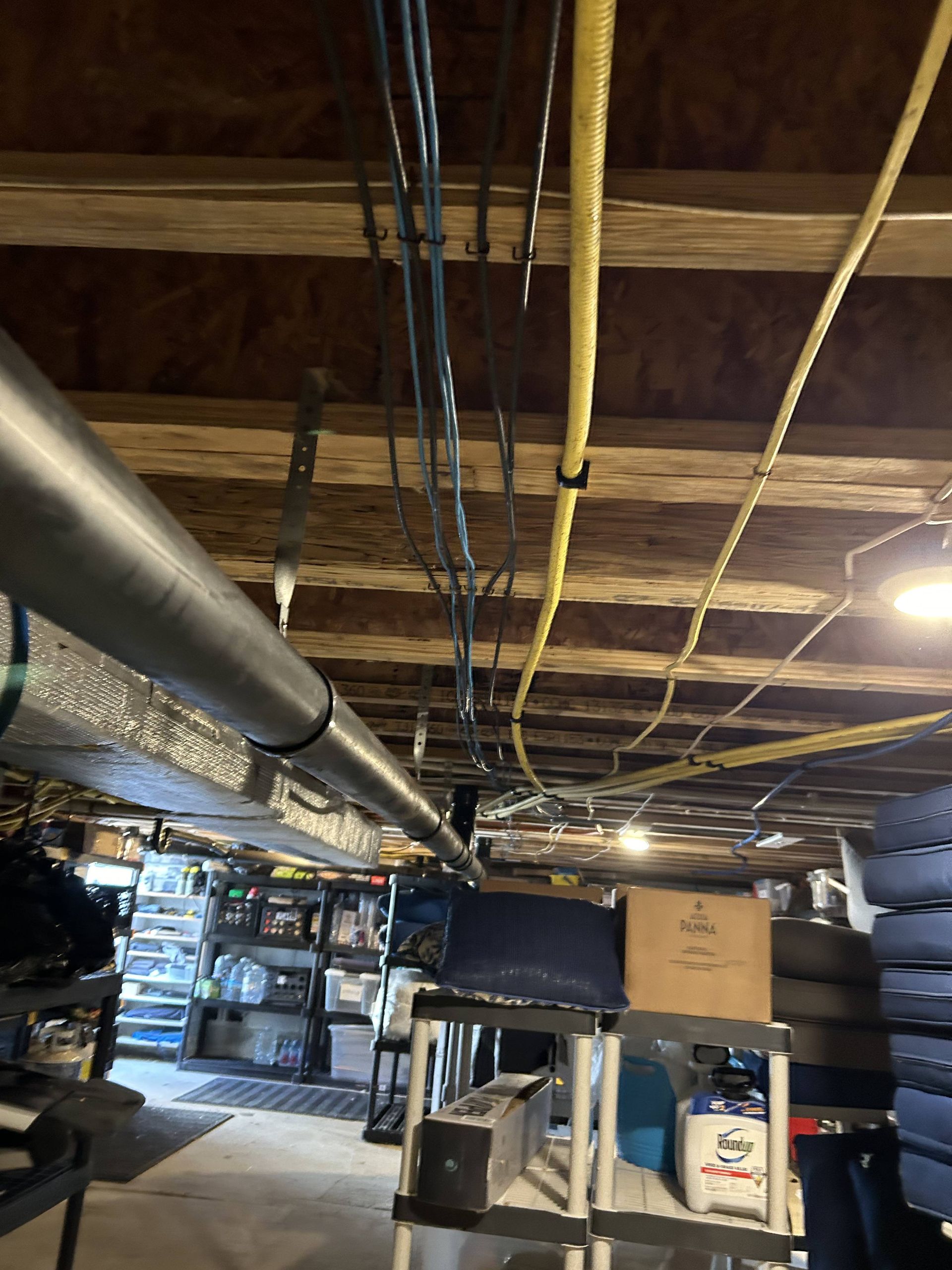Basement storage area with exposed ceiling beams, pipes, shelving, and boxes.