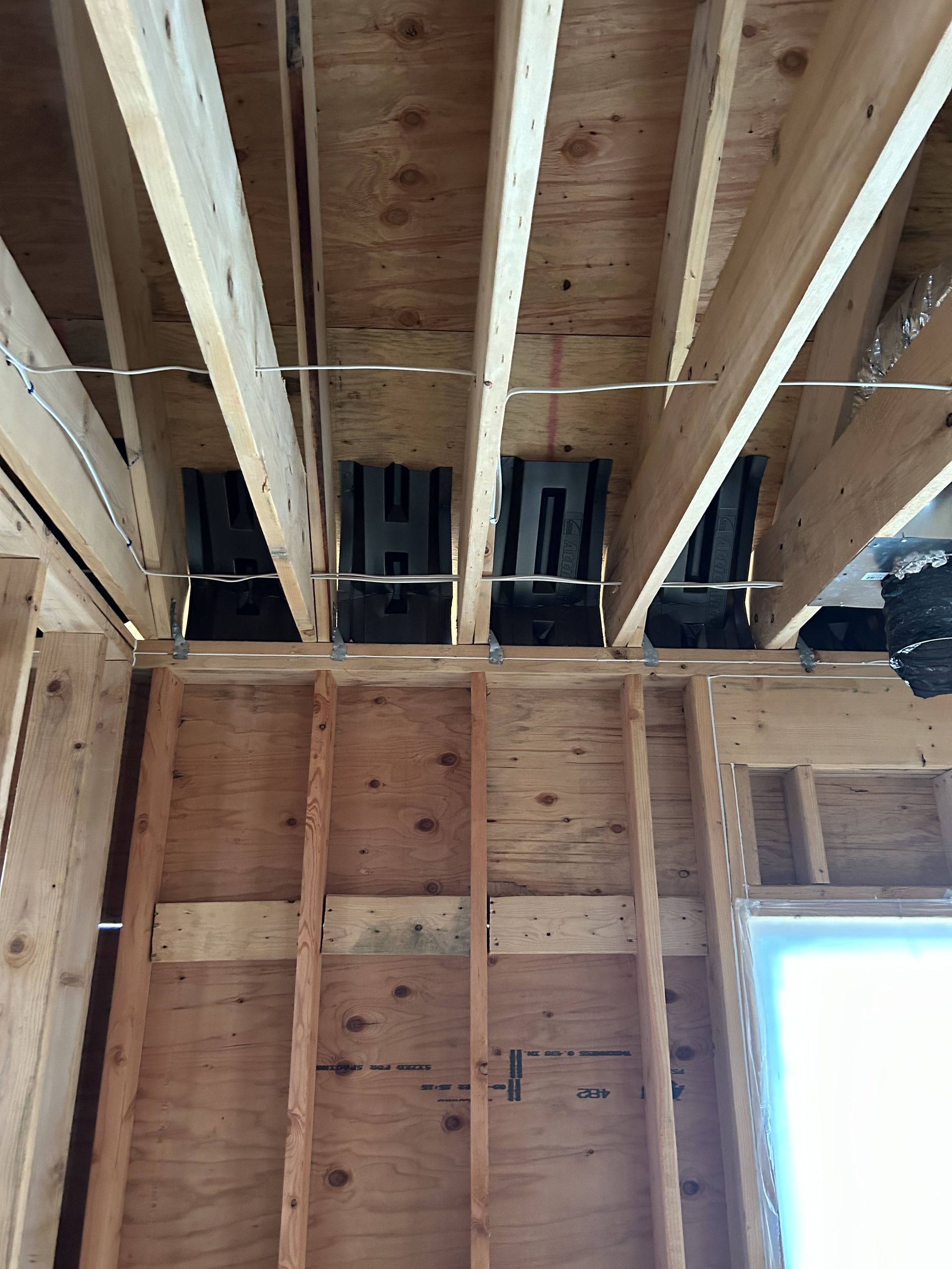 Exposed wooden ceiling framing in an unfinished room with a bright window on the right