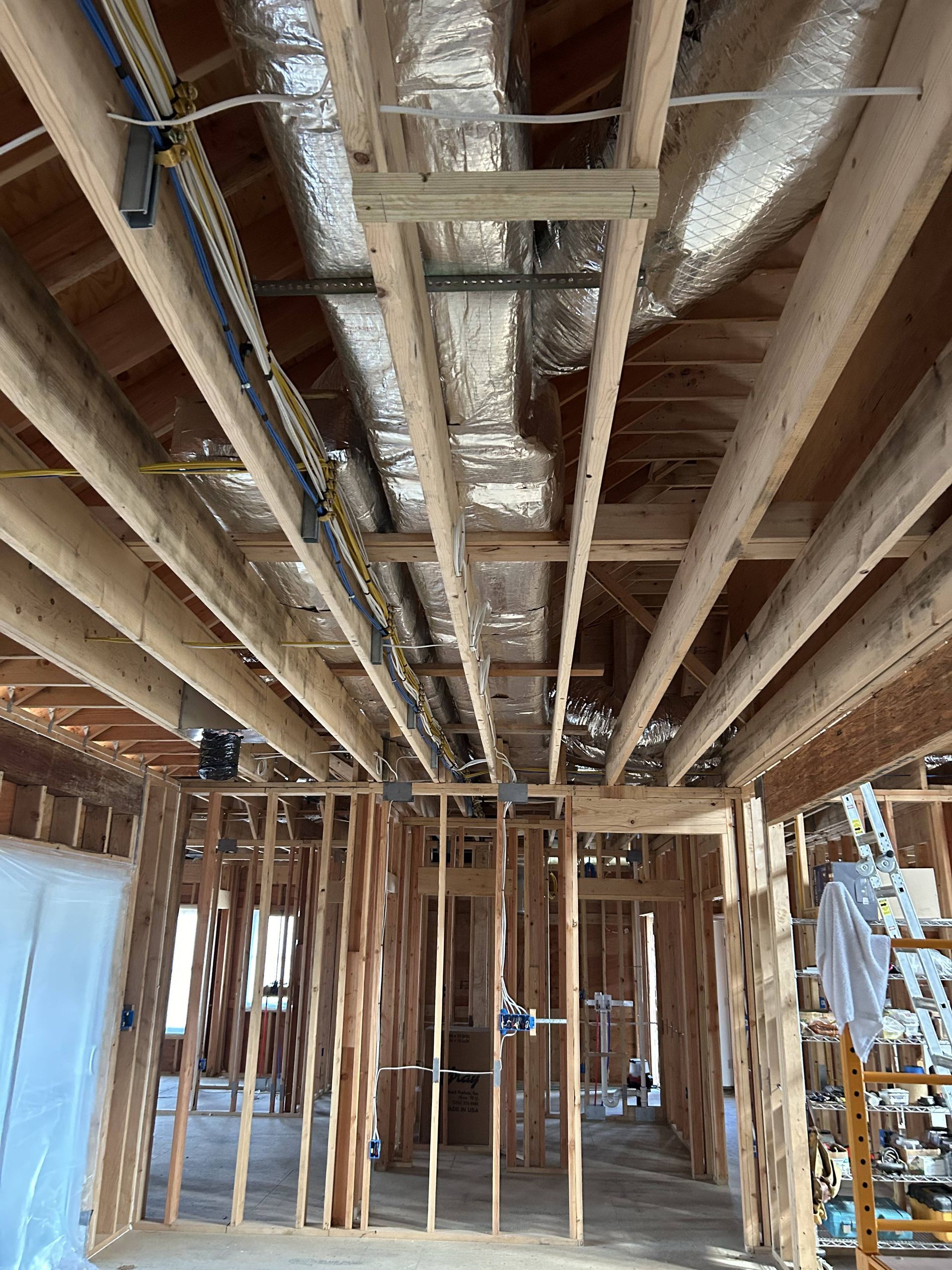 Unfinished basement framing with exposed ceiling joists, ductwork, and wiring under construction.