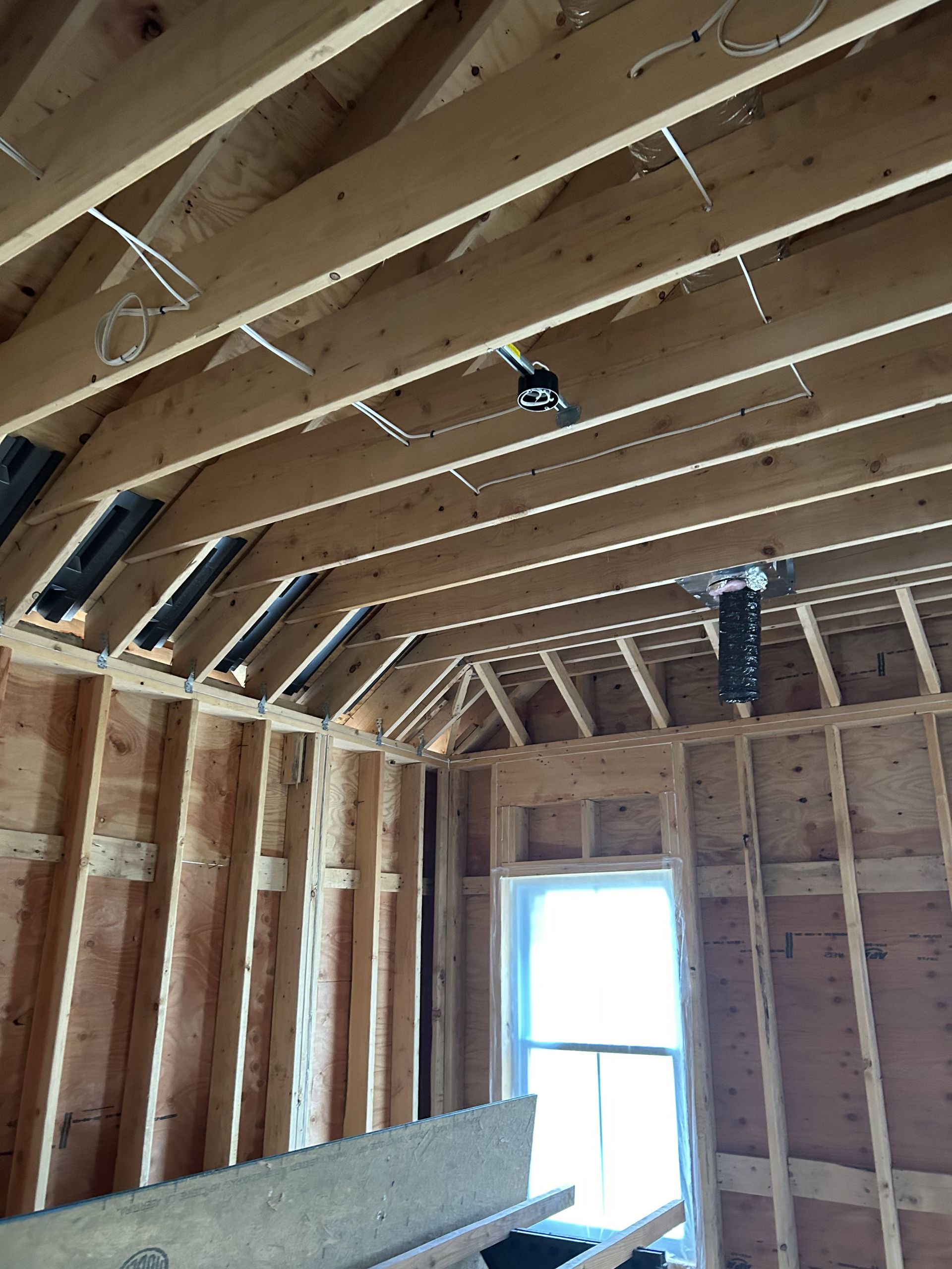 Unfinished room with exposed wood framing, sloped ceiling, and a bright window at the far end