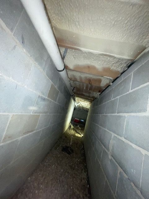 Narrow basement corridor with cinder block walls, damaged ceiling, and debris on the floor