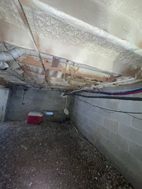 Crawlspace with insulated ceiling, cinderblock walls, gravel floor, and a red cooler on the ground