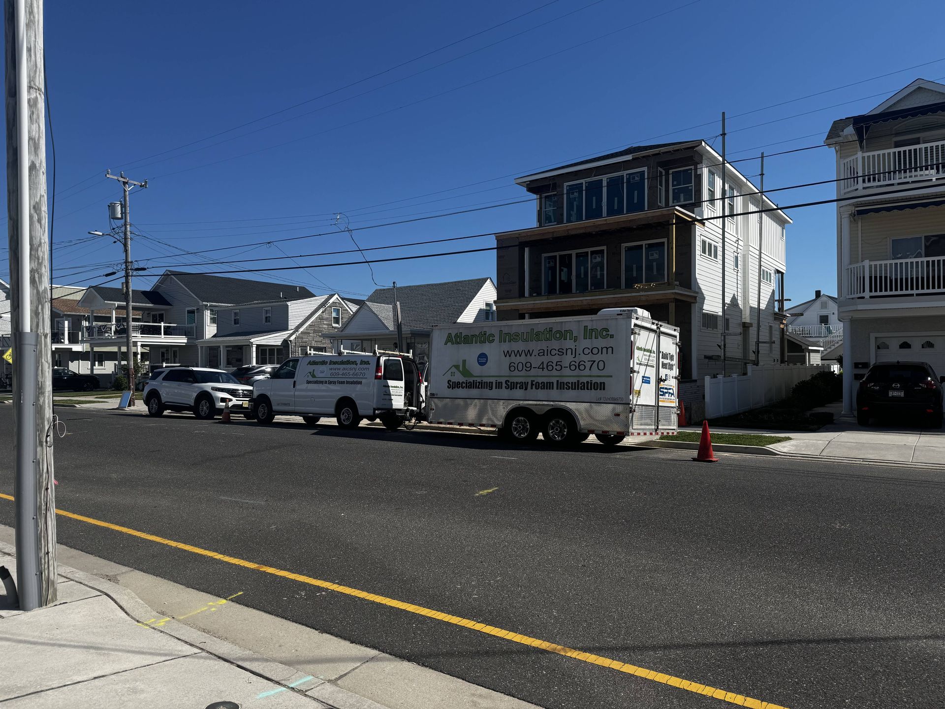 Moving truck and van parked on a sunny street beside houses and a sidewalk