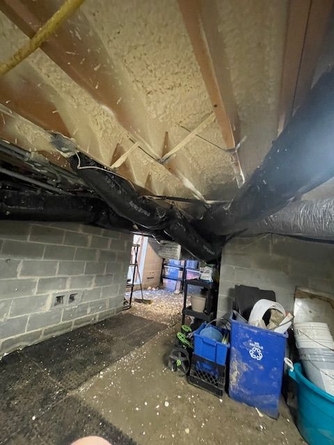 Moldy crawlspace with black plastic tarp, exposed joists, cinder block wall, and storage bins on the floor