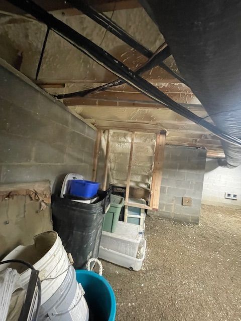 Storage area under a wooden structure with bins, barrels, and cinder block walls