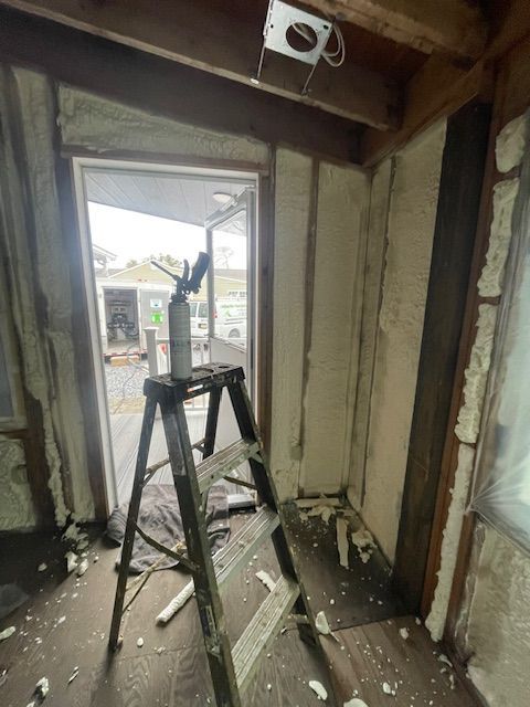 Partially renovated room with a ladder, exposed framing, and a window opening to the outside