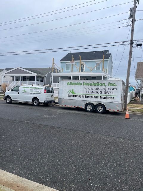 Two white service vans parked on a wet street under gray skies, one with landscaping business signage.