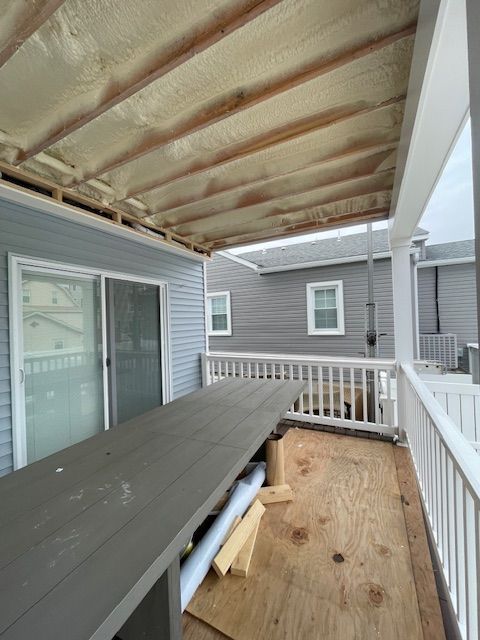 Covered backyard deck with gray siding, sliding door, and unfinished wooden flooring under a pergola-like roof.
